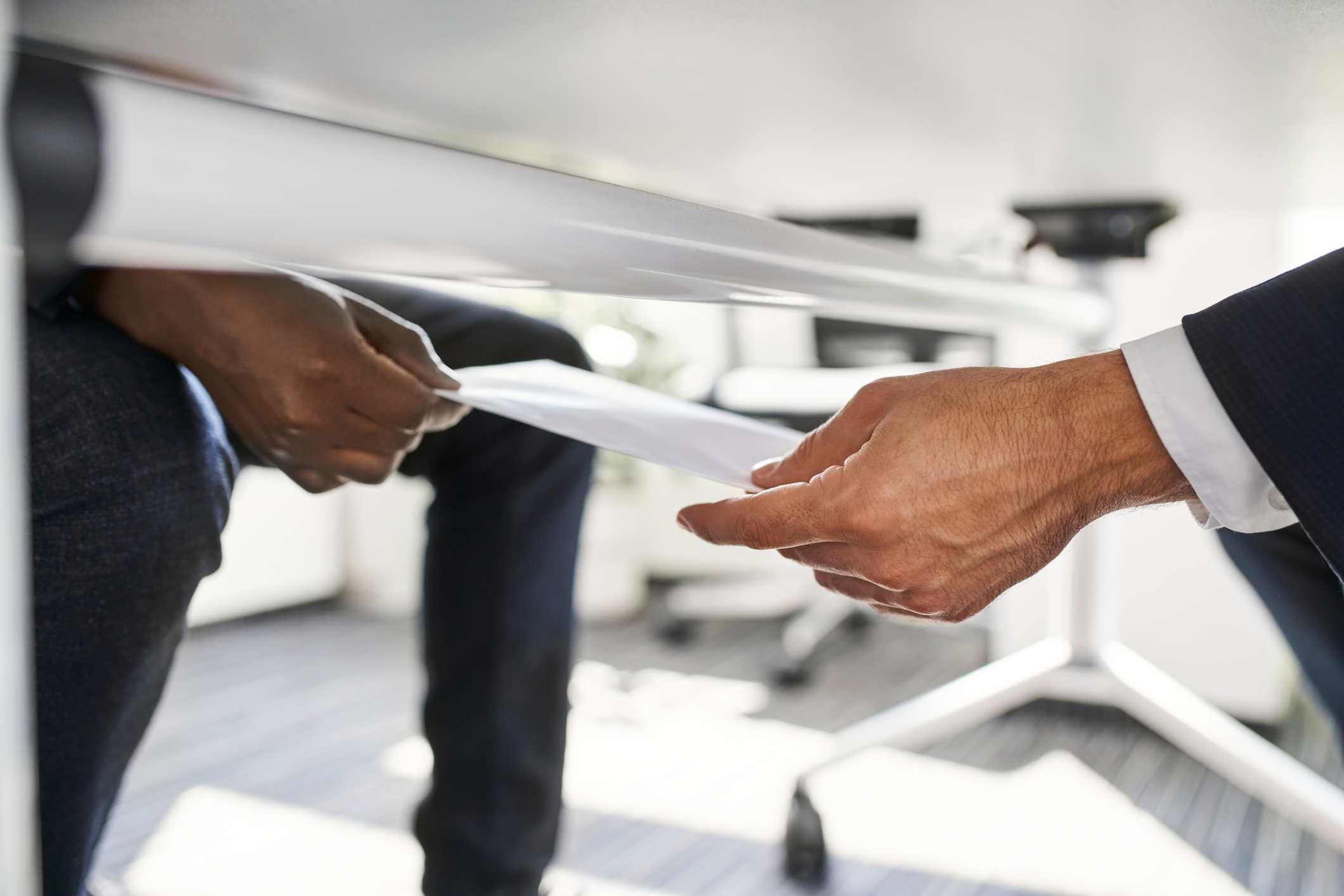 Two individuals exchanging an envelope discreetly under a table, symbolizing corruption.